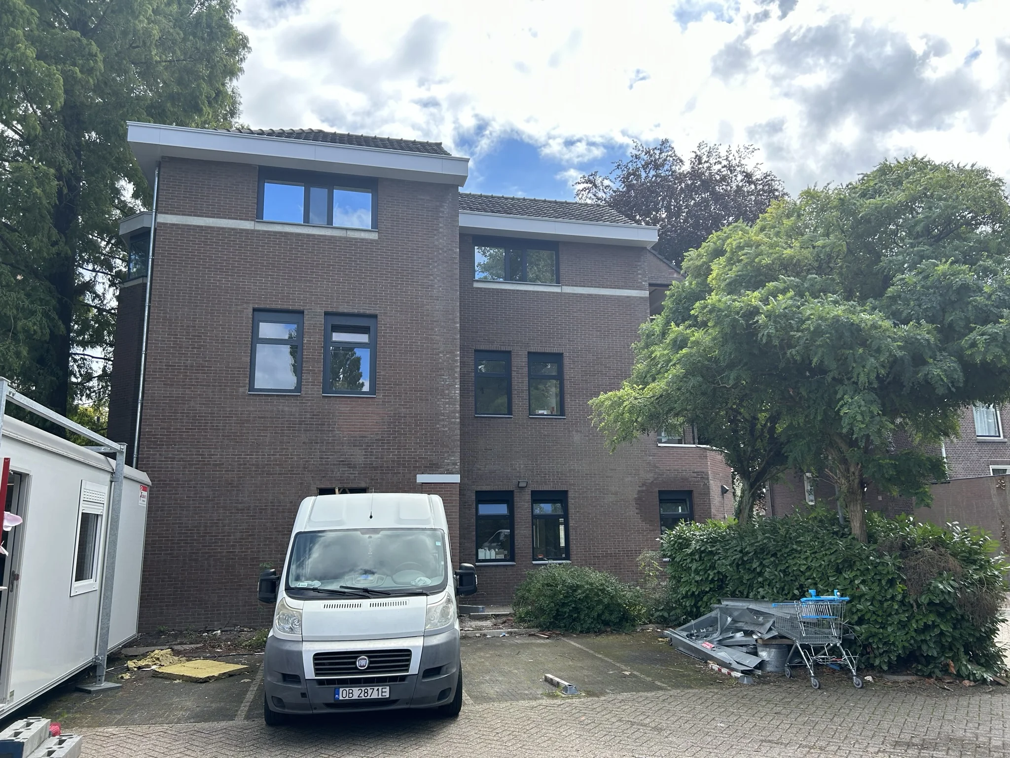 Bakstenen appartementsgebouw aan de Bergse Dorpsstraat met een geparkeerde witte bestelbus en winkelwagen op de voorgrond.